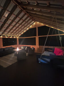 Covered outdoor living space with fire pit, seating, and swing bed at Riddle Road